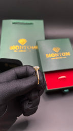 BIONTOMのゴールドモアサナイトリング。黒い手袋をした手で持ち、背景にはブランドのギフトボックスとショッパーが見えるサイドビュー。