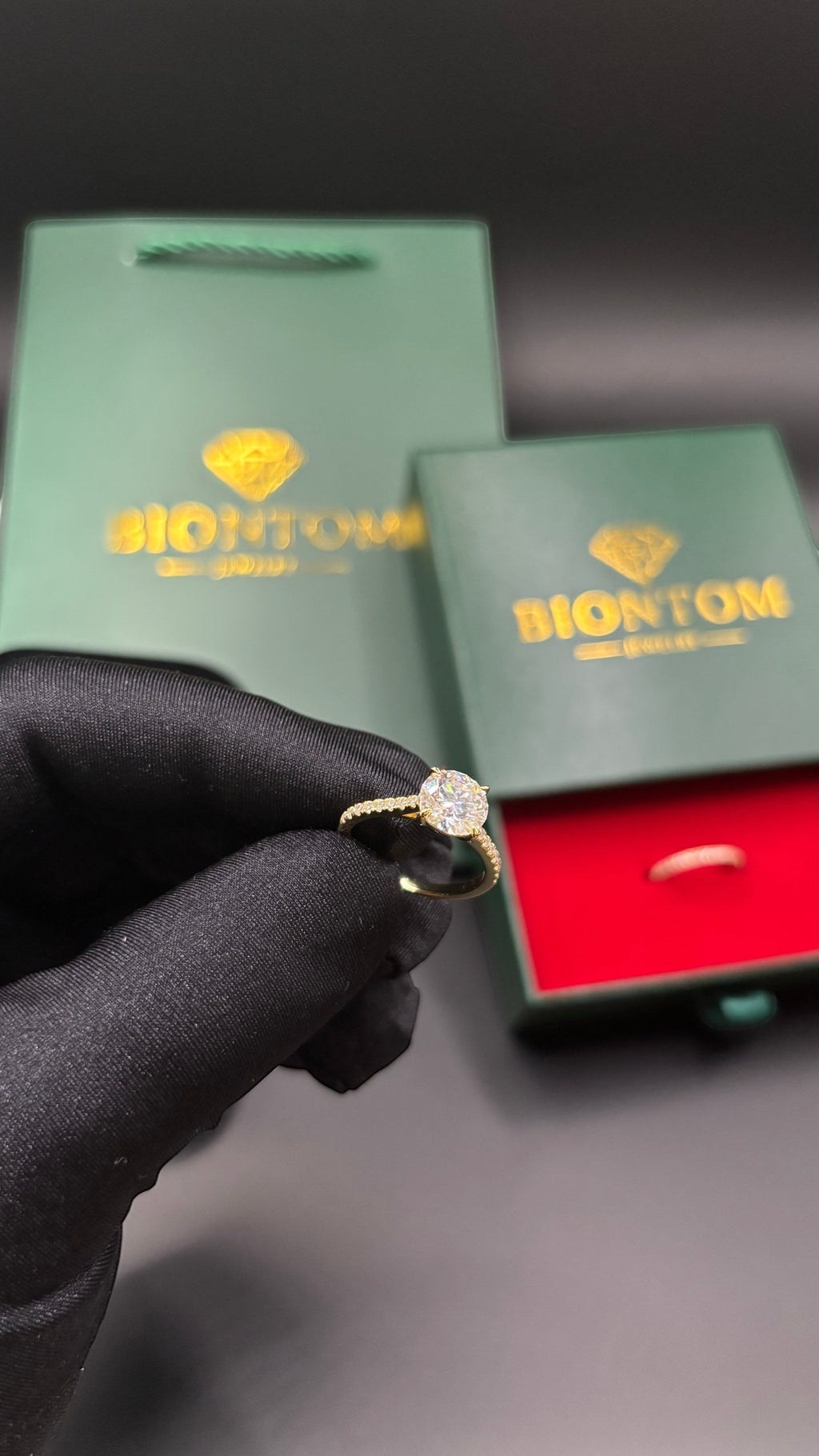 BIONTOMのエレガントなモアサナイトリングセット。ゴールドの台座に大粒の石が輝き、ギフトボックスとショッパーが添えられた高級感あるデザイン。